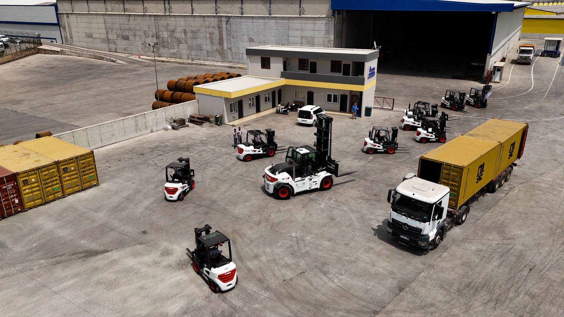 Aerial view of industrial yard with forklifts, containers, and truck.