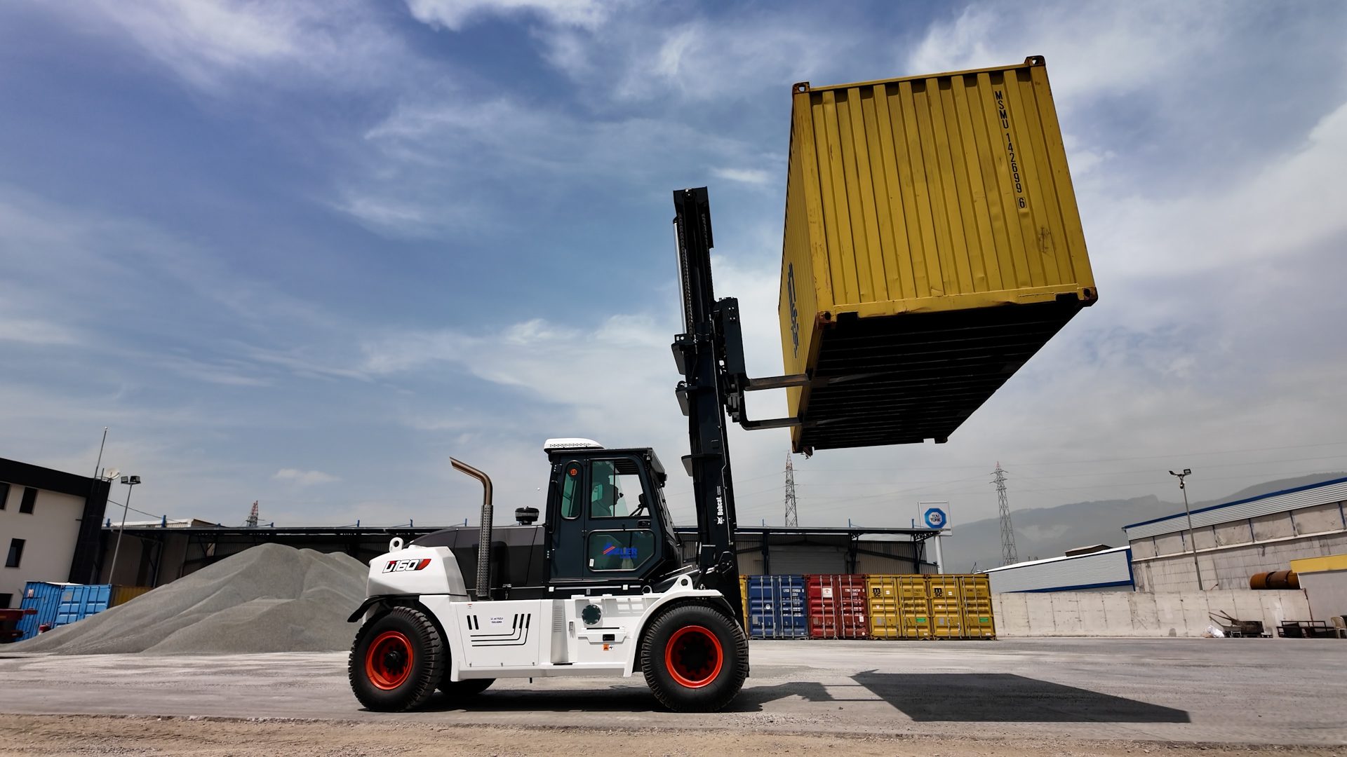 White forklift lifting yellow shipping container in industrial yard.