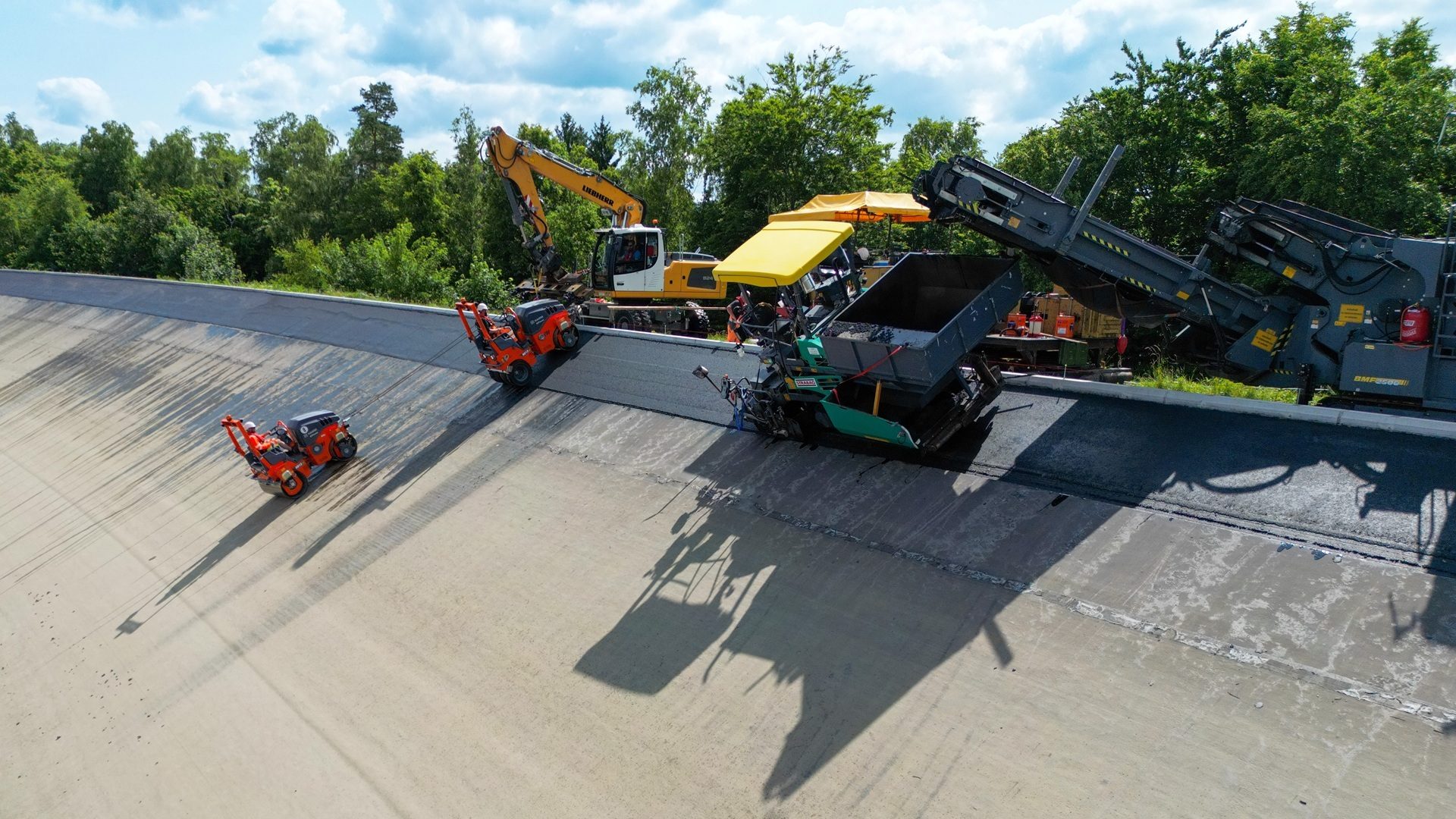 Construction crew paving a steep embankment with asphalt using various machinery.
