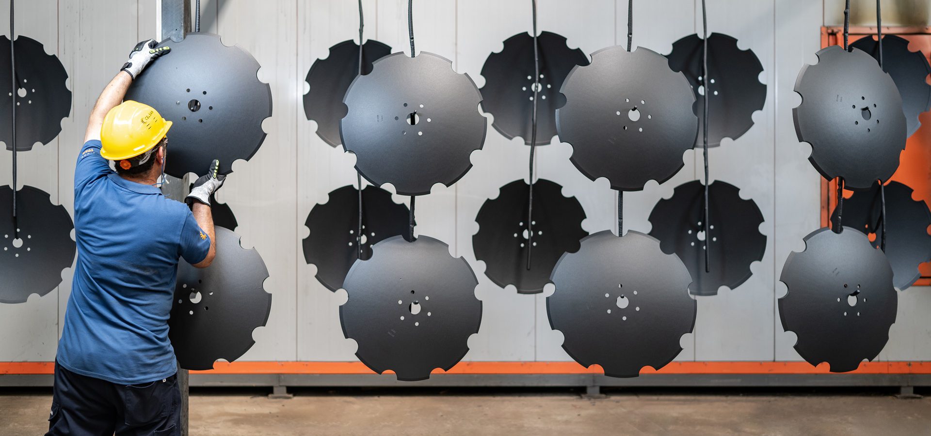 Worker handling notched industrial discs, some hanging, in a factory setting.