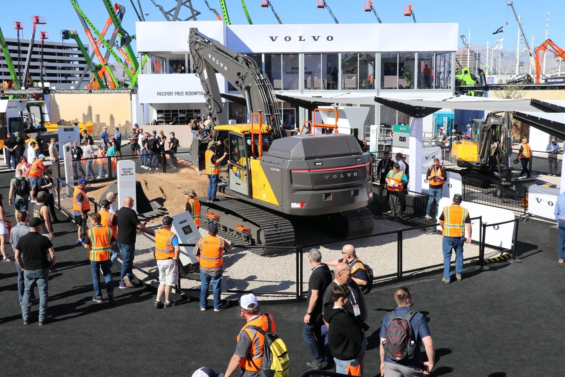 A Volvo construction equipment display with a large yellow and gray excavator, people, and the Volvo building.