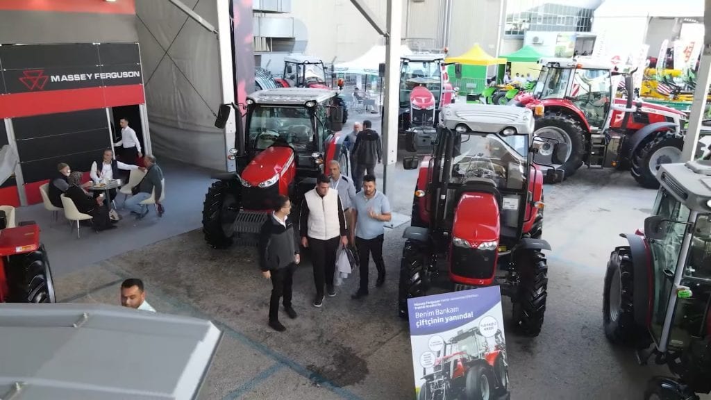 People browse red Massey Ferguson tractors at an indoor agricultural exhibition.