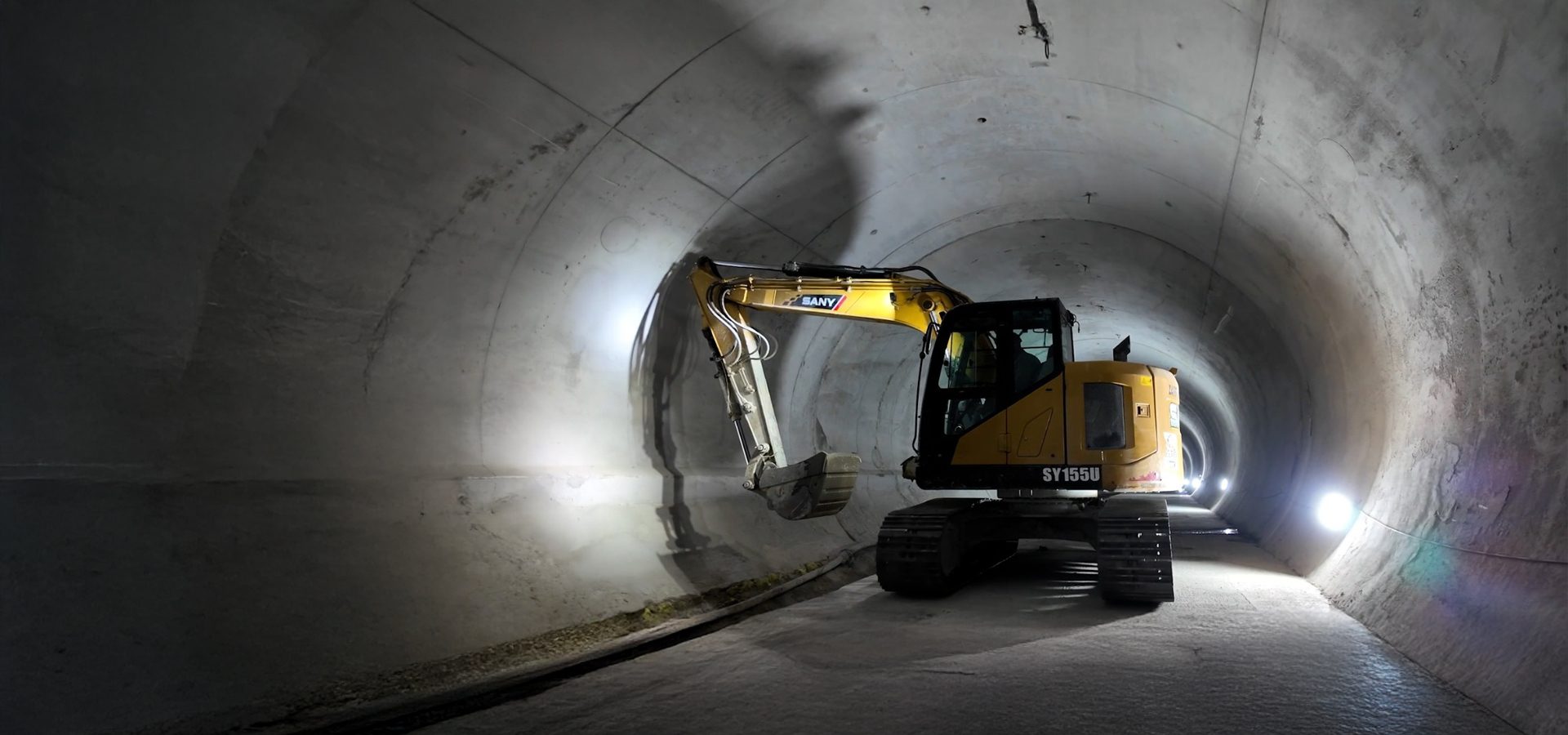 Yellow SANY SY155U excavator in a concrete tunnel with lights.