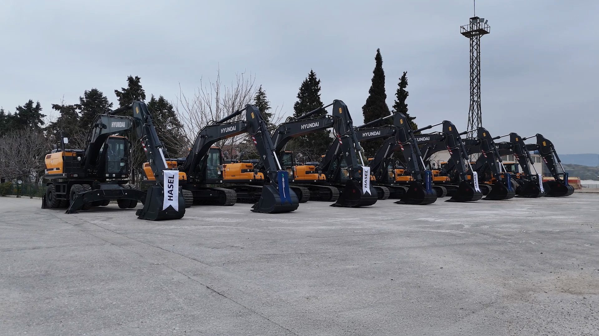 A line of new dark gray and yellow Hyundai excavators with "HASEL" banners on a paved lot.