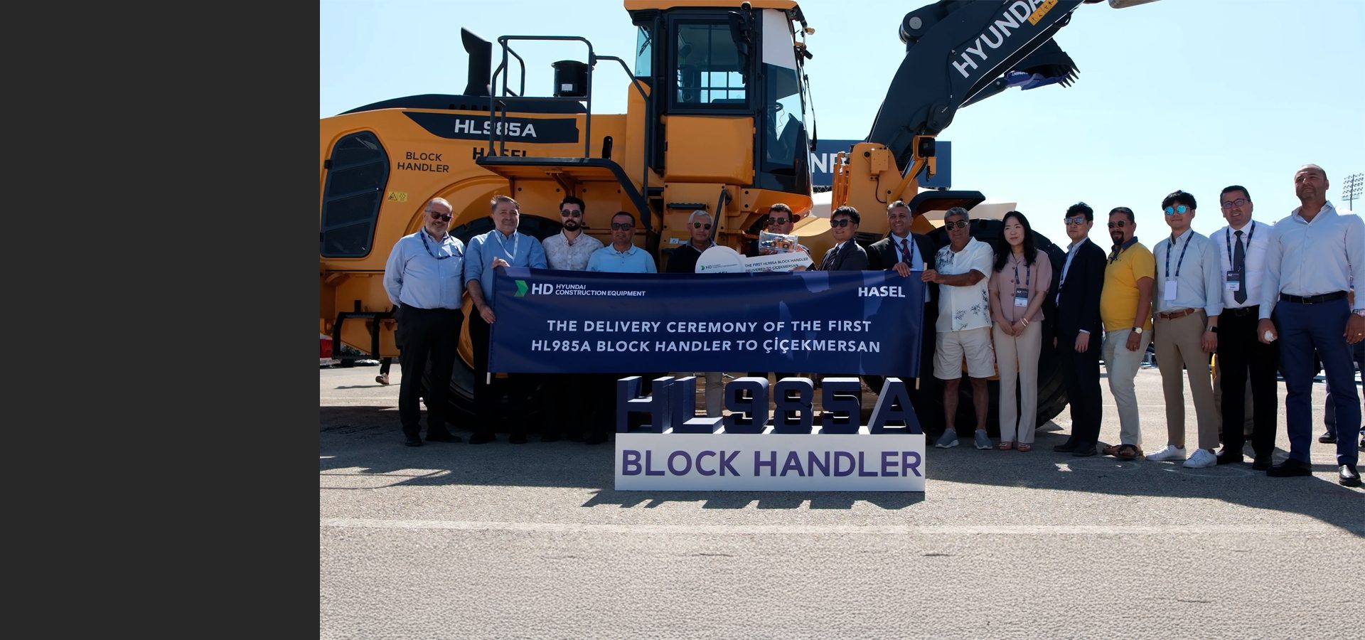 Delivery ceremony of a Hyundai HL985A Block Handler with a group of people and a banner.