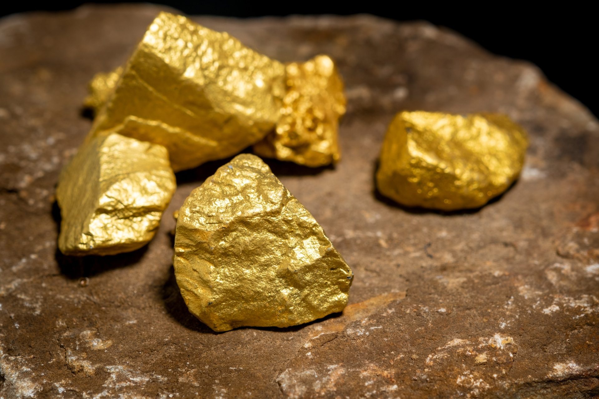 Several bright gold nuggets resting on a dark, textured rock surface.