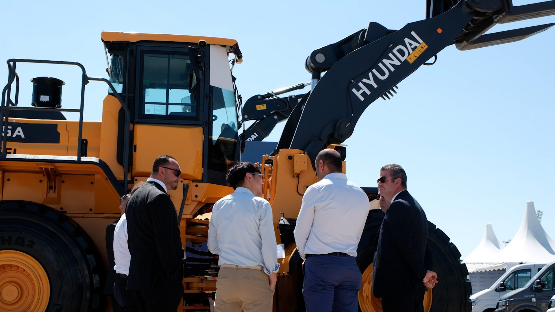 A group of men stand around a large yellow Hyundai heavy machine under a clear sky.