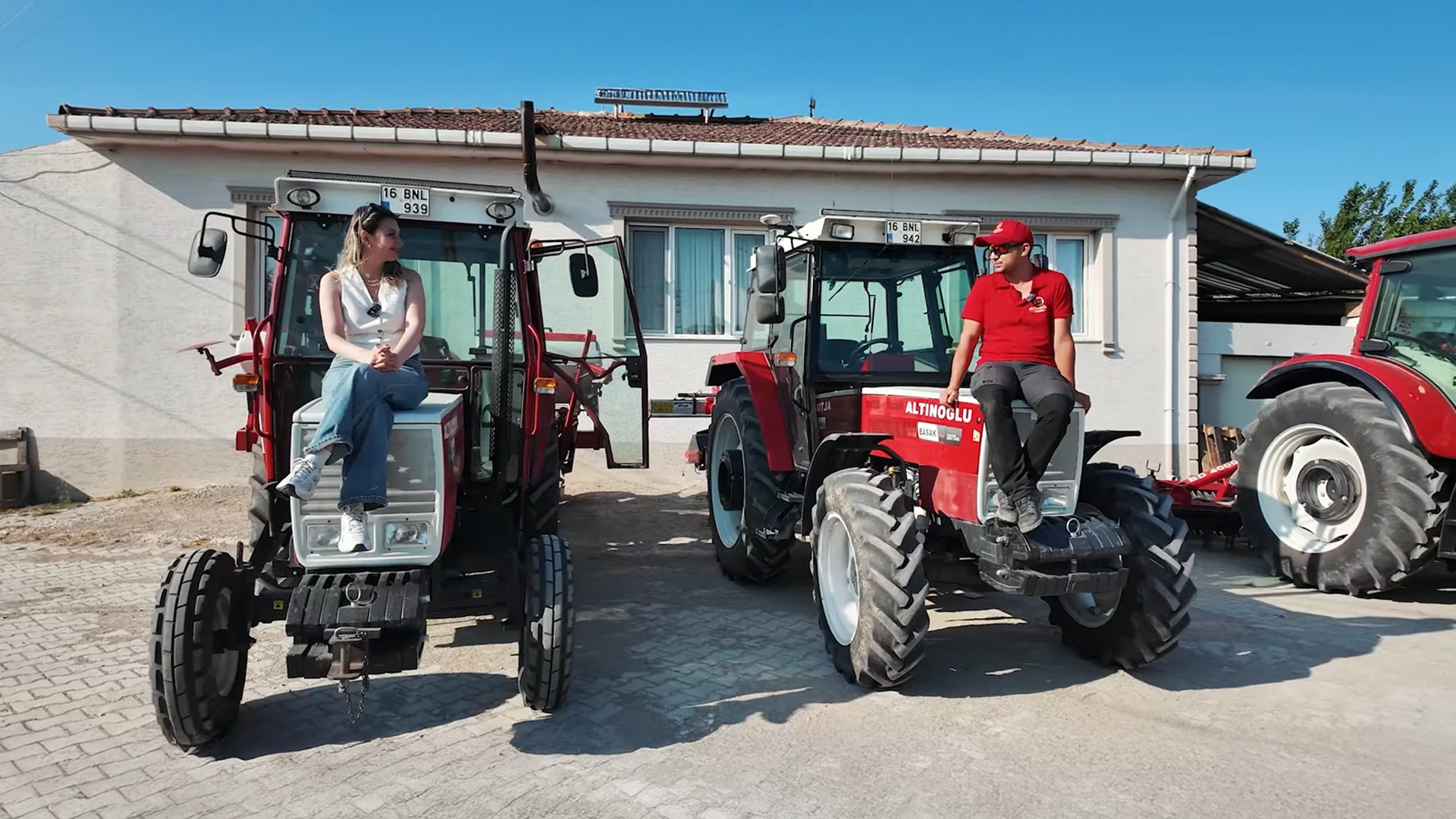 A man and a woman sitting on red tractors outside a house.