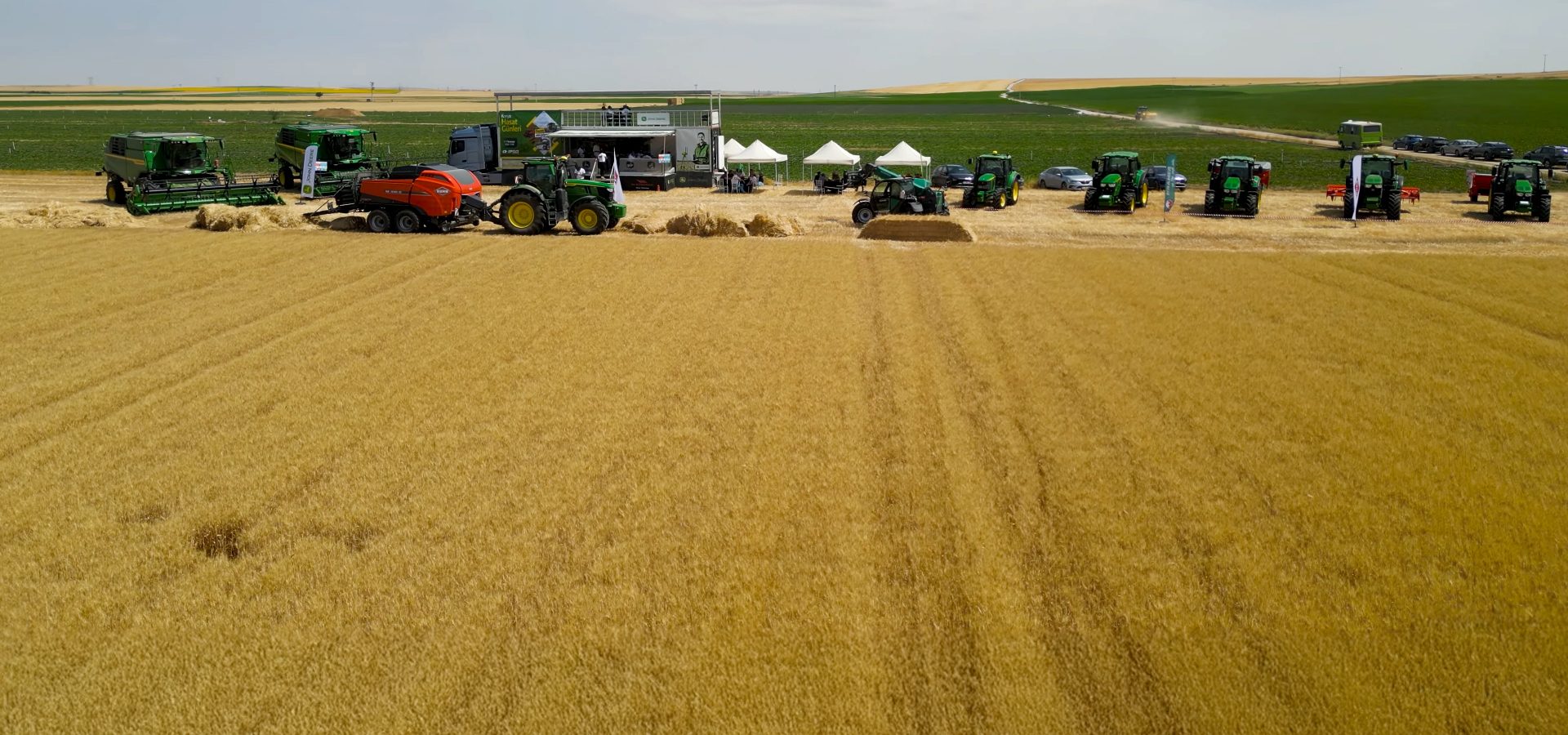 Agricultural equipment display with combines, tractors, and tents in a vast golden wheat field.