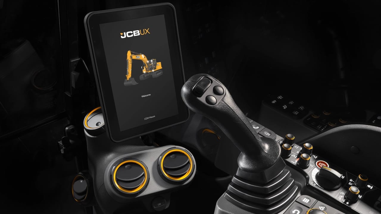 Close-up of a JCB UX digital display and control stick in a heavy machinery cockpit.
