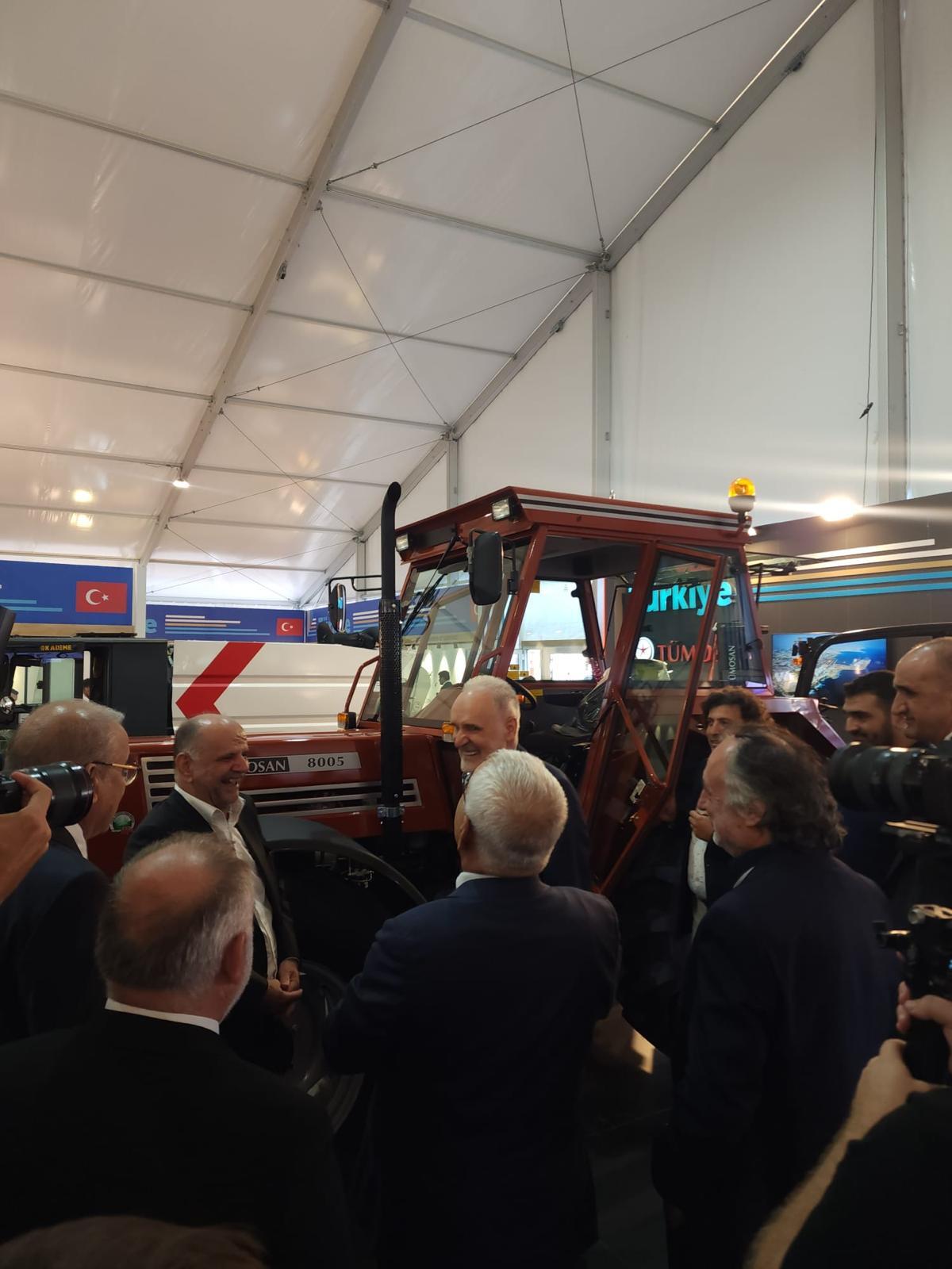 Men gathered around a red tractor inside a tent, with a Turkish flag visible.