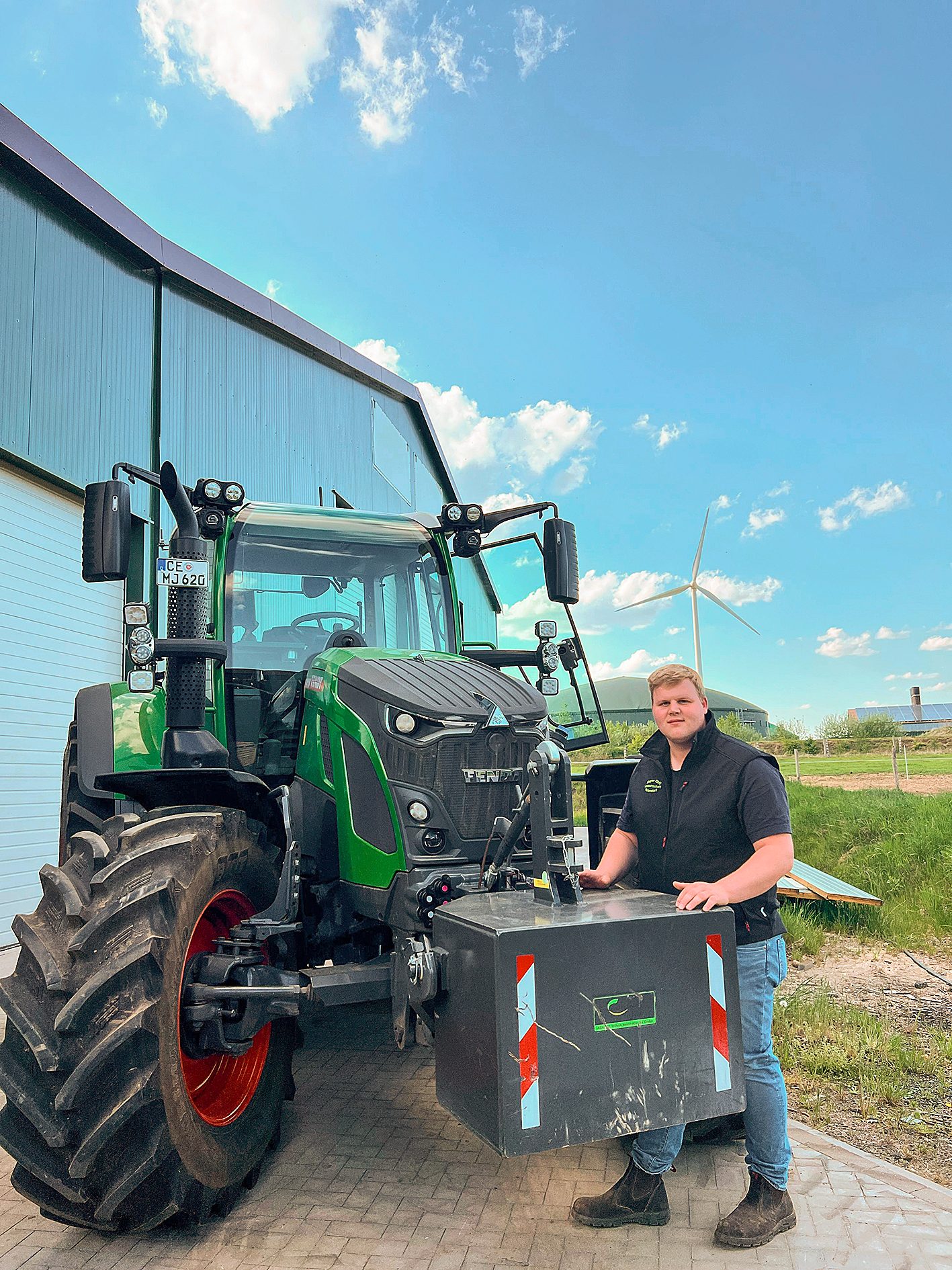 Man by green tractor with wind turbine.