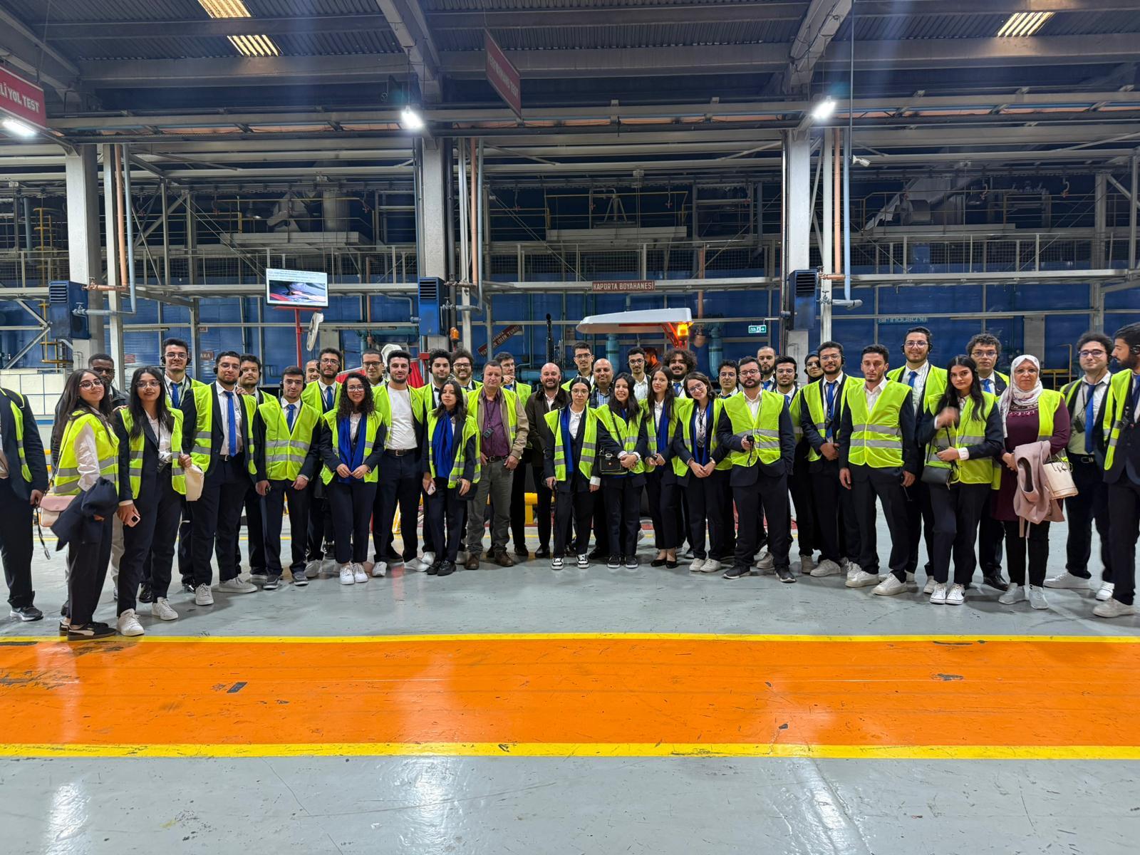 A large group of people in bright safety vests posing inside a factory.