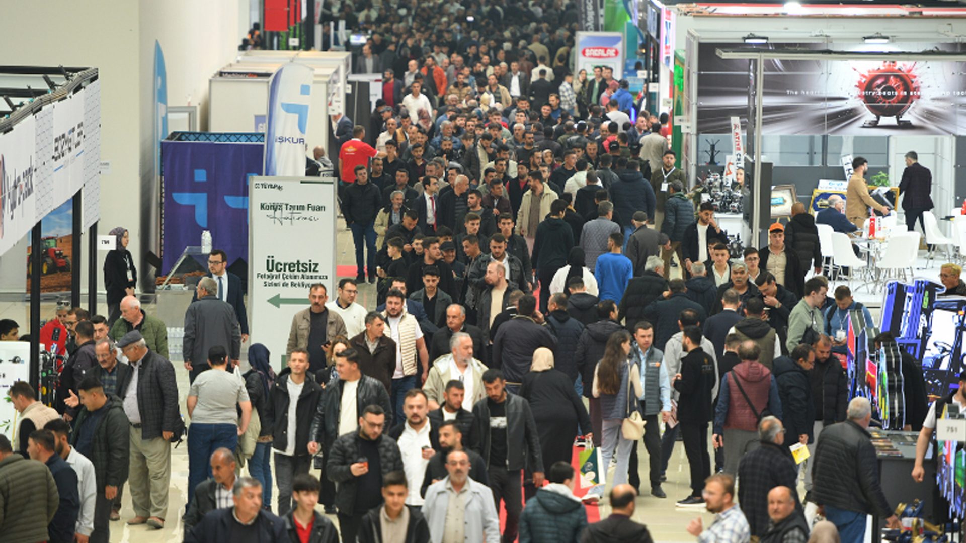A very crowded indoor event with many people walking through aisles at a trade show or exhibition.