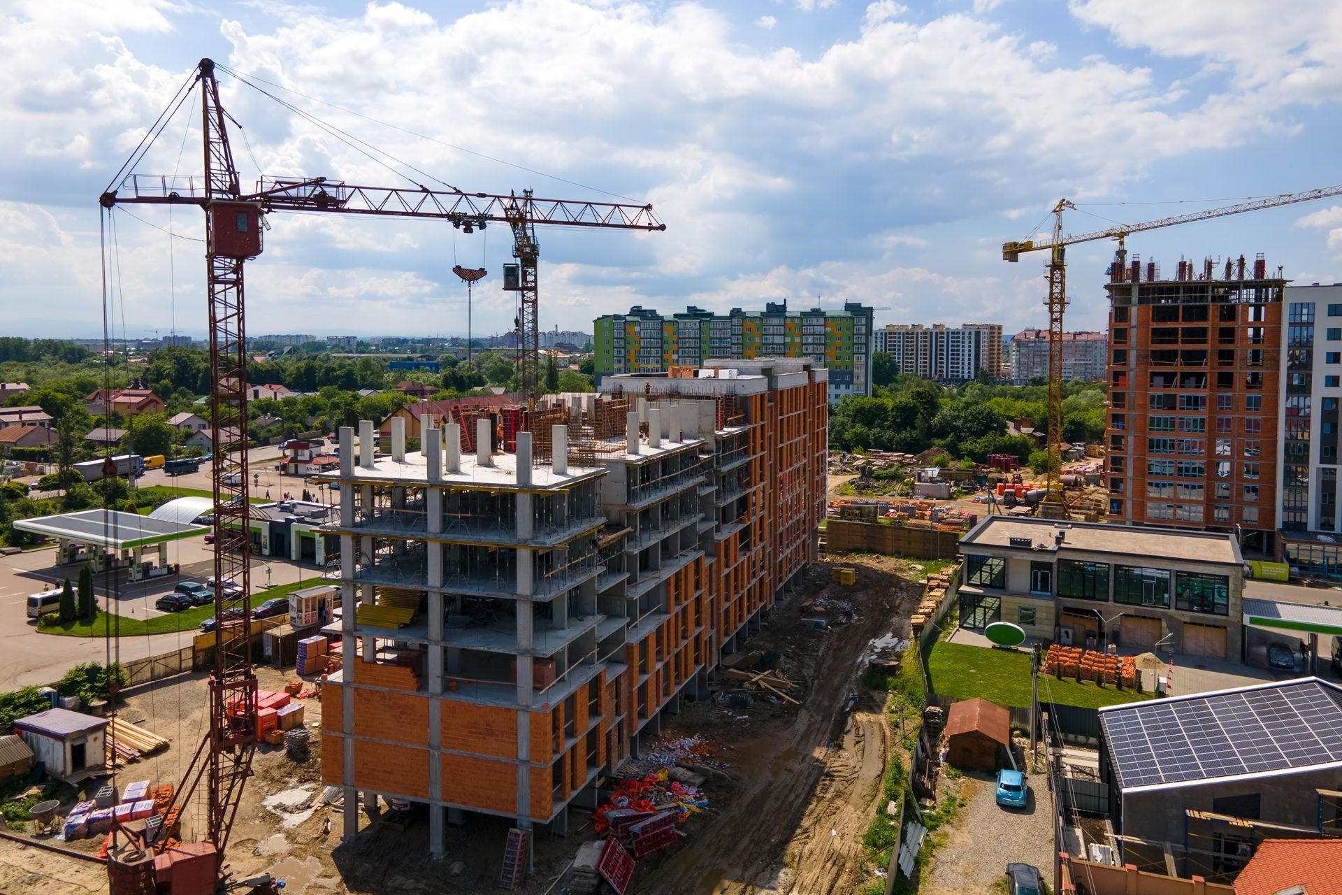 Aerial view of a construction site with multiple tower cranes, partially built buildings, and city in background.