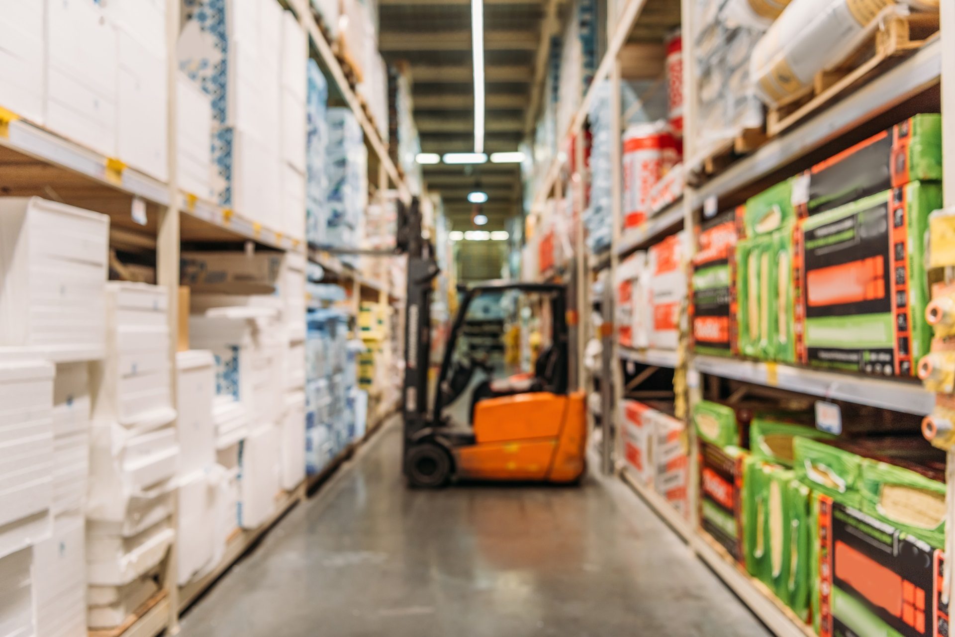 Blurry image of a warehouse aisle with stocked shelves and an orange forklift.