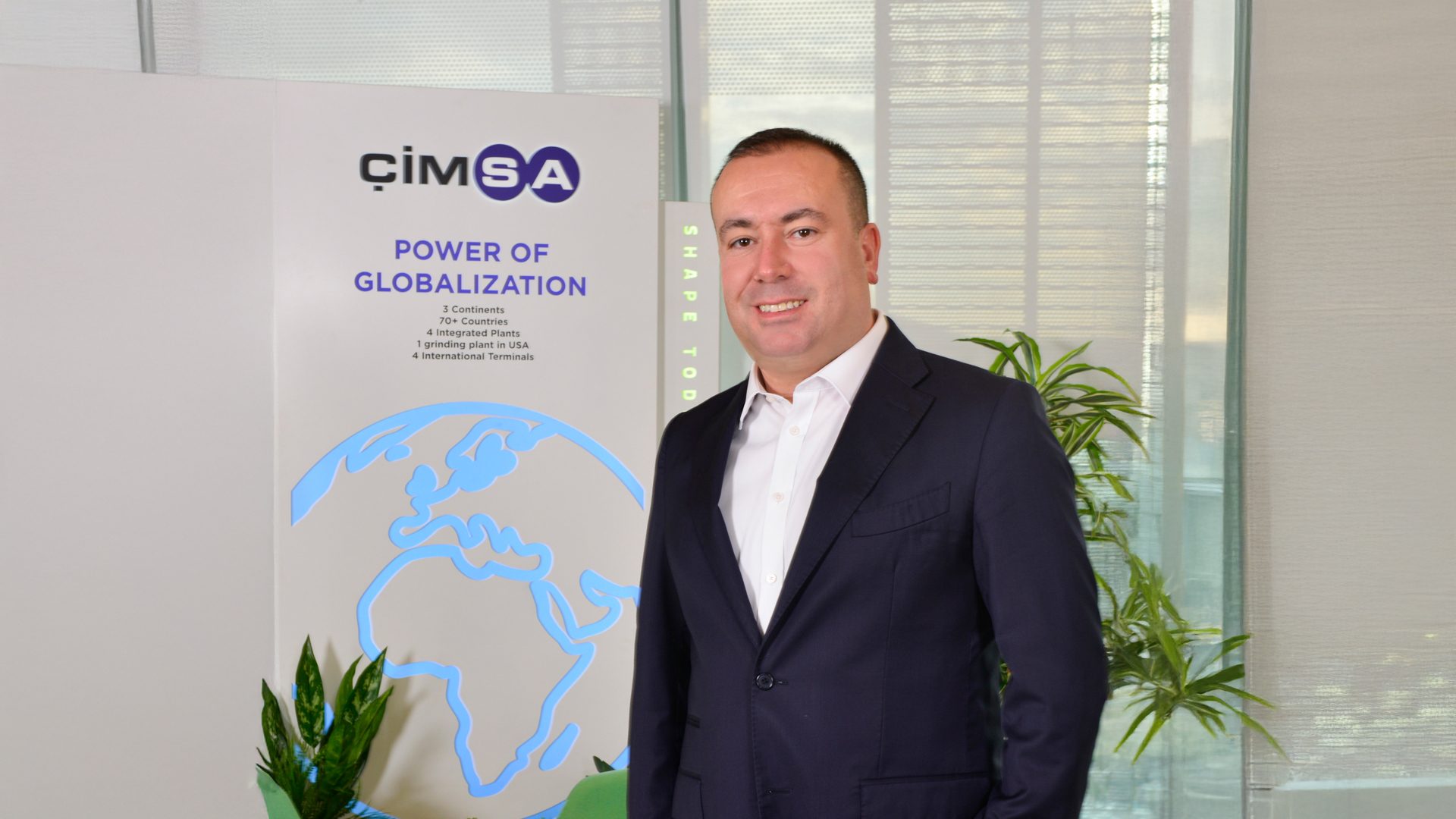 Man smiling in suit next to ÇİMSA 'POWER OF GLOBALIZATION' display with world map.