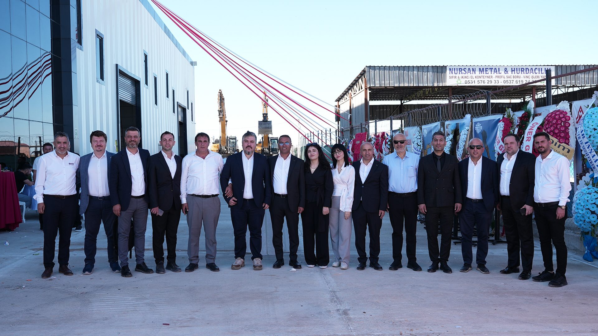 A group of people, including men and women, at the opening of Nursan Metal & Hurdacılık with ribbons.