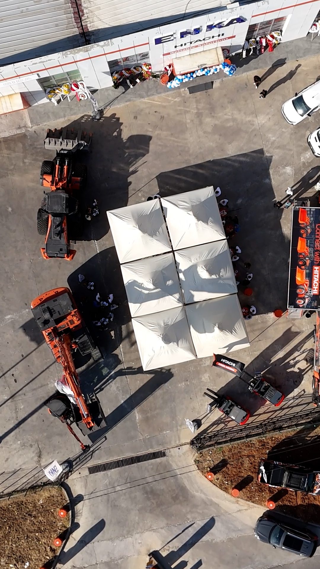 Aerial shot of a Hitachi equipment event with excavators, tents, and people.