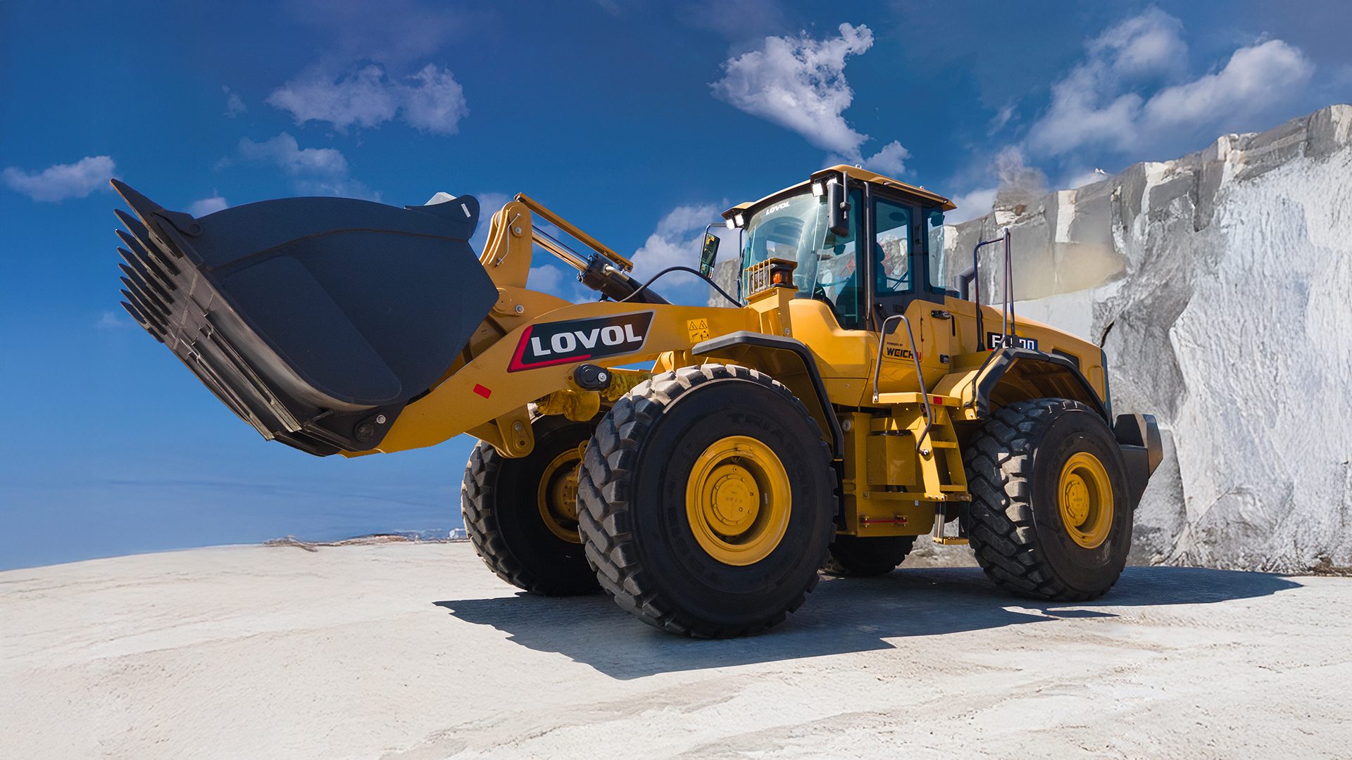 Yellow Lovol wheel loader with raised bucket in a quarry, under a blue sky.