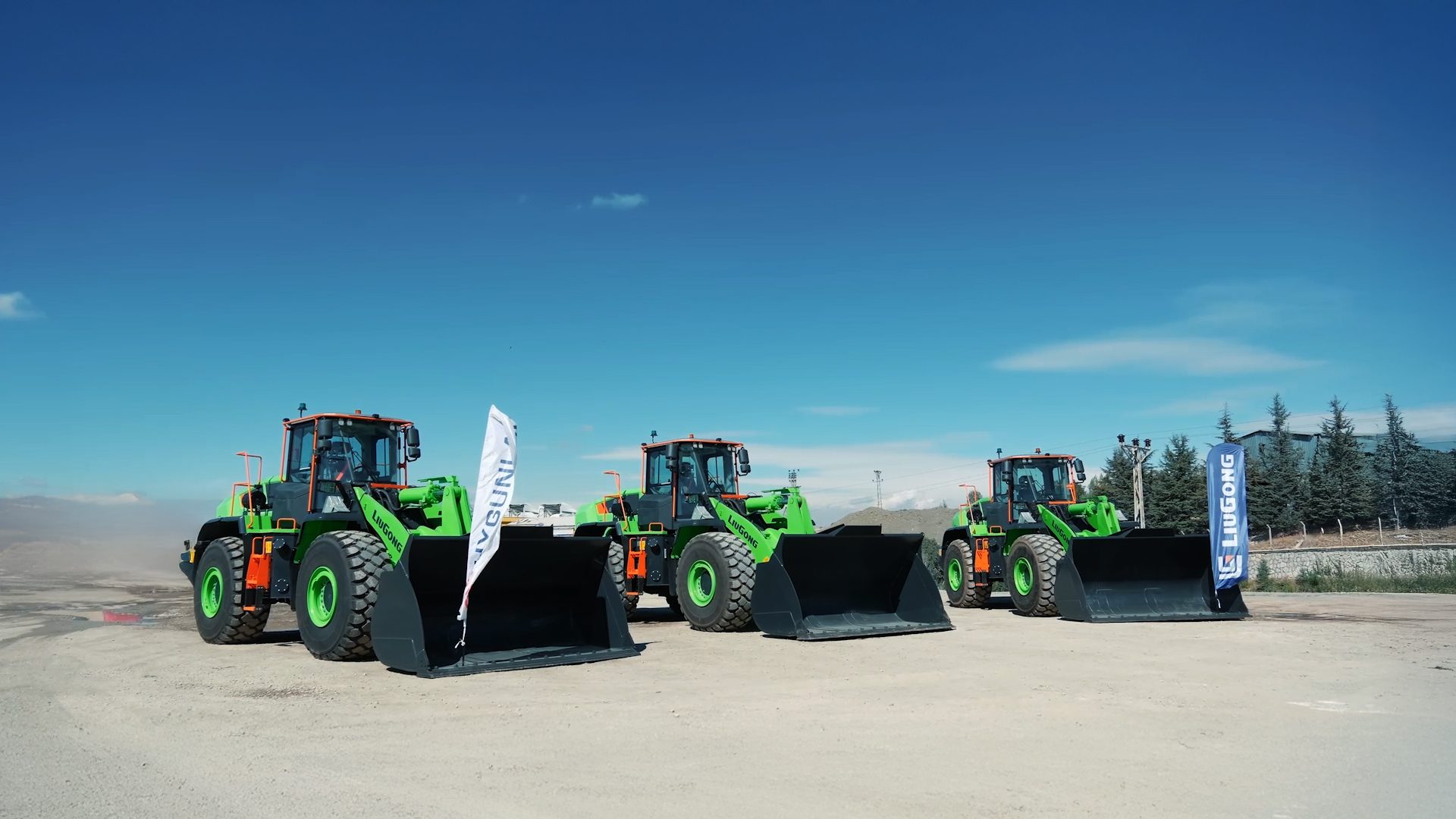 Three green and black Liugong wheel loaders parked on a dirt lot under a blue sky.