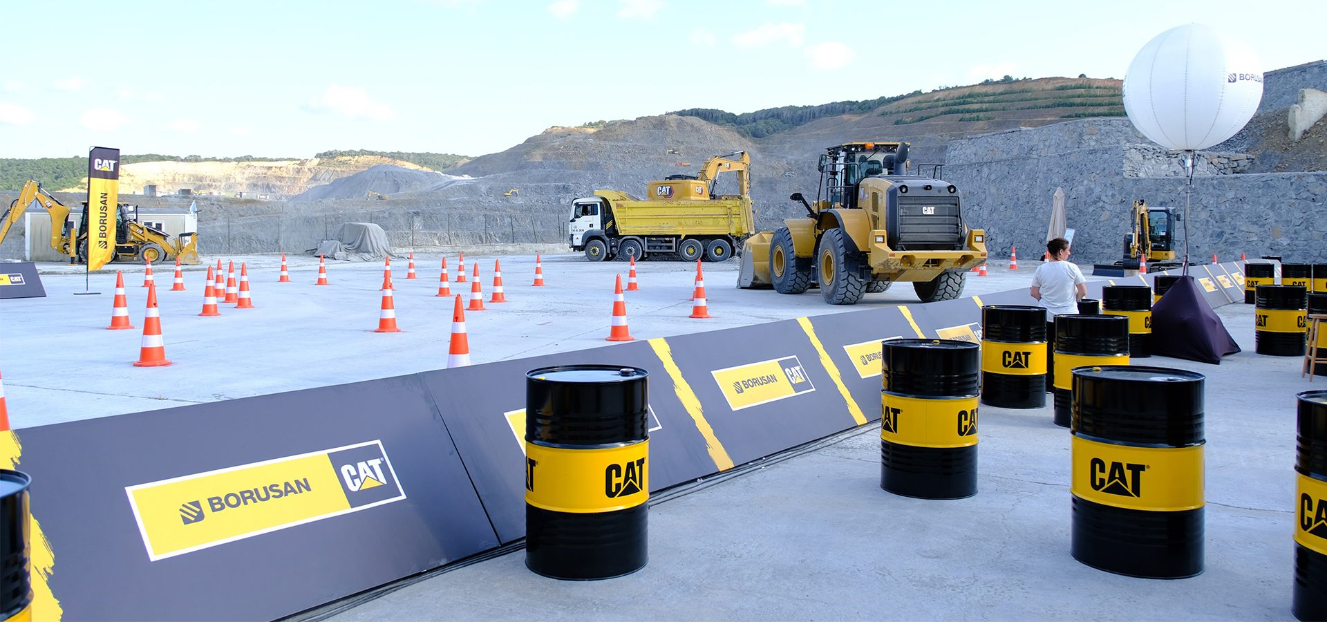 CAT heavy machinery, cones, and branded barrels at a construction site demonstration.