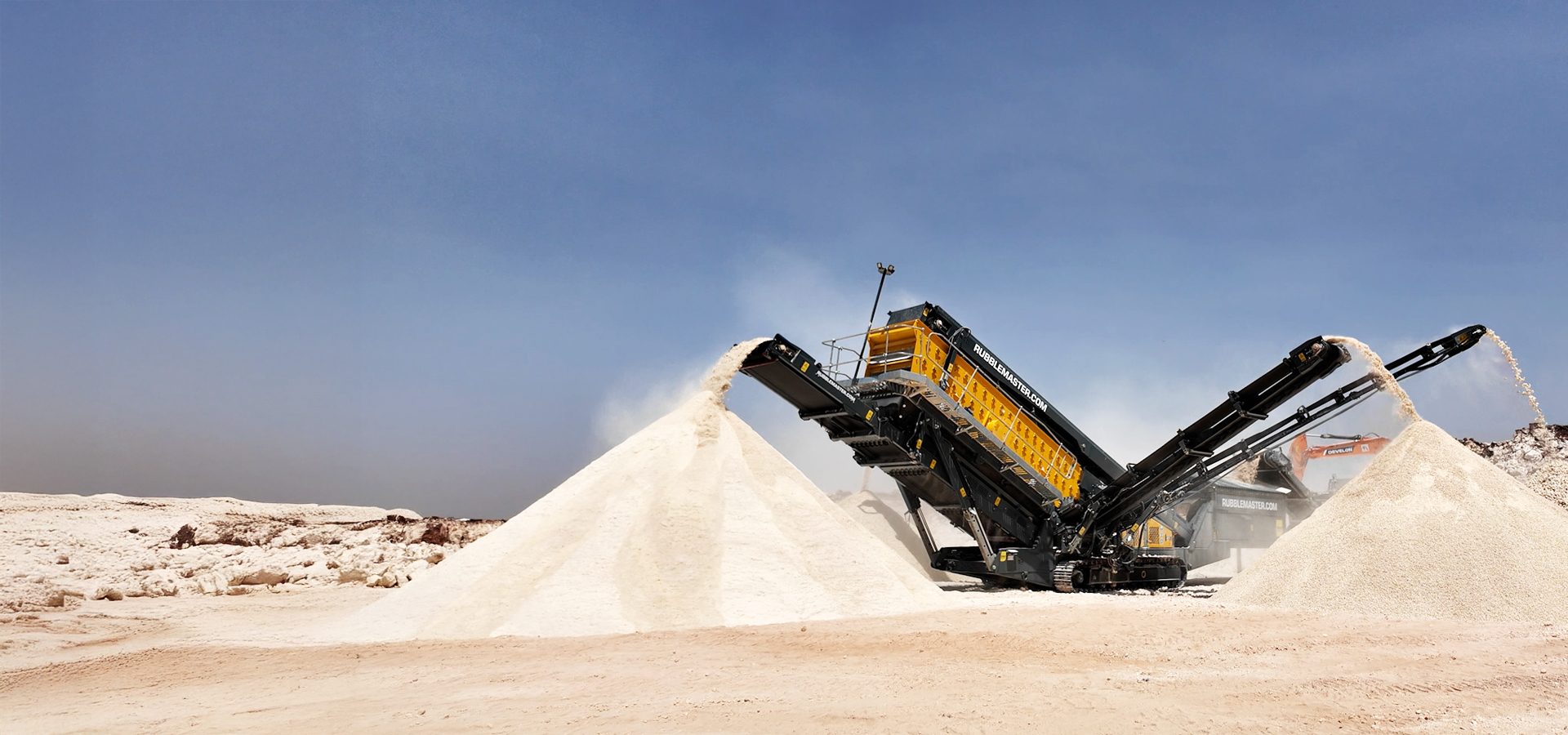 Mobile crushing and screening plant creating piles of aggregate under a clear sky.