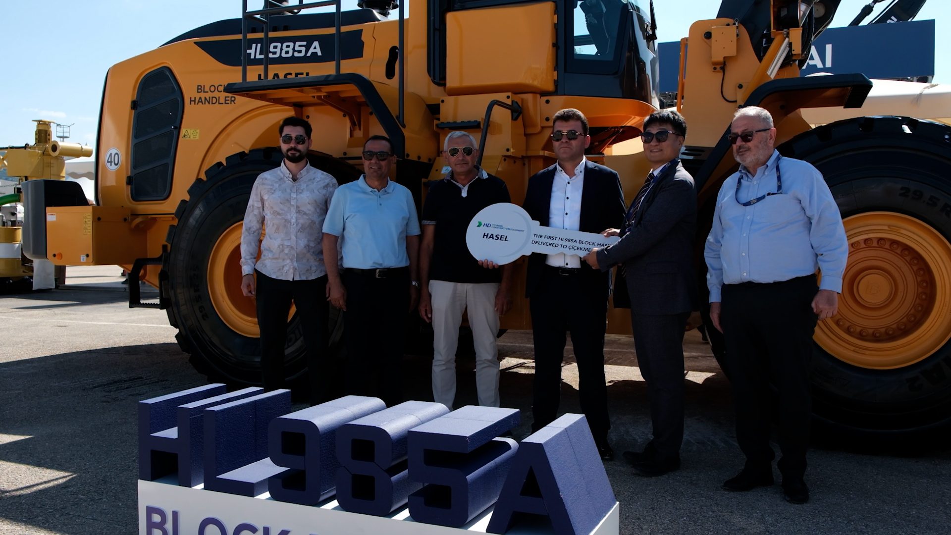 Men at a key exchange ceremony for a large yellow HL985A Block Handler machine.