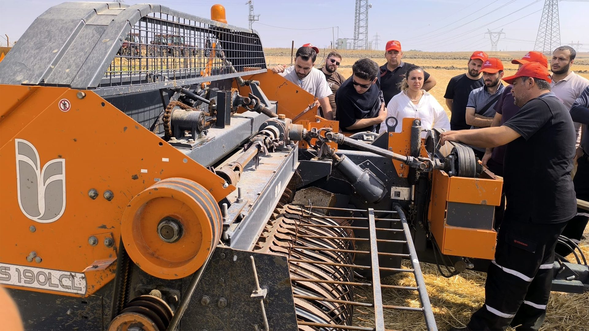 Group of people inspecting an orange farm machine in a field, with one man pointing out details.