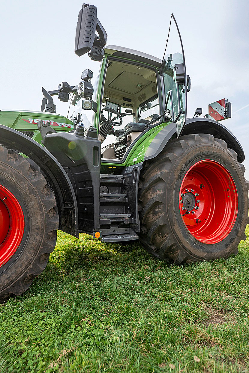 Green Fendt tractor on grass, showing its cab, steps, and red wheels.