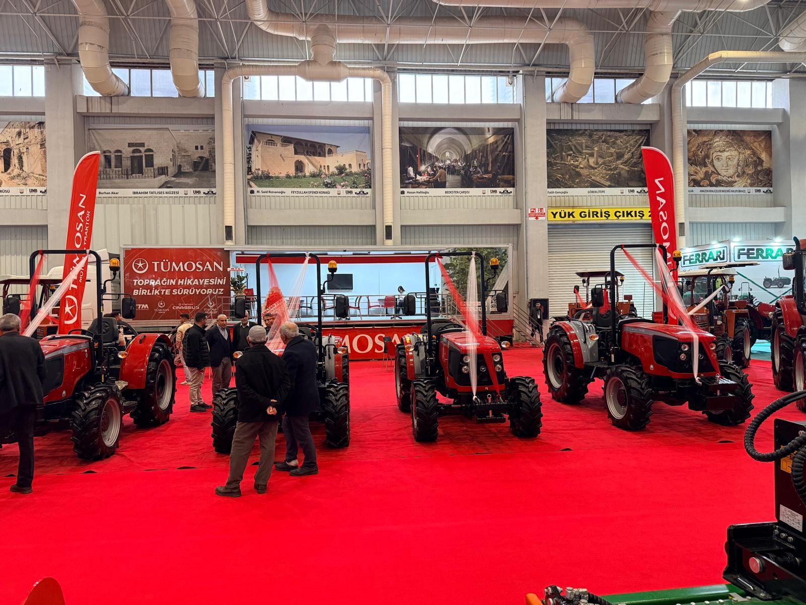 TÜMOSAN tractors on a red carpet at an indoor exhibition, with people and wall murals.