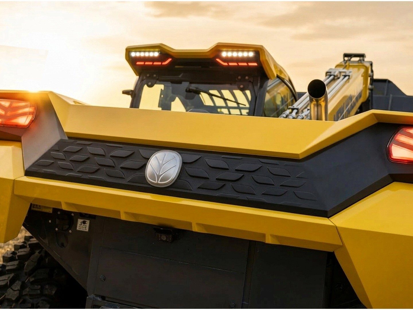 Rear view of a yellow heavy-duty vehicle with a black textured panel and emblem.