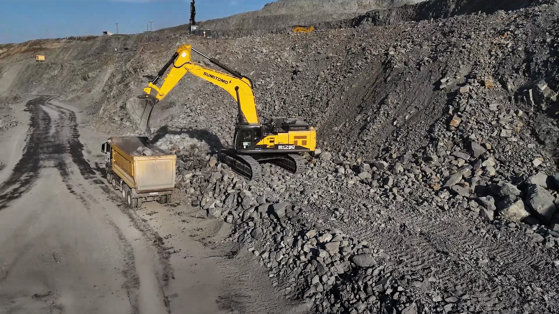 Yellow excavator loads rocks into a dump truck in a rocky quarry.