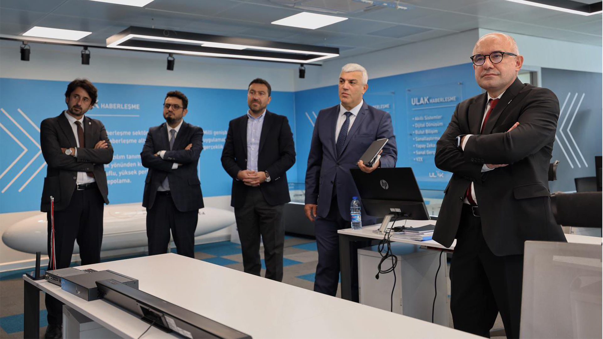 Five men in suits stand in a modern office with "ULAK HABERLEŞME" on the blue wall.
