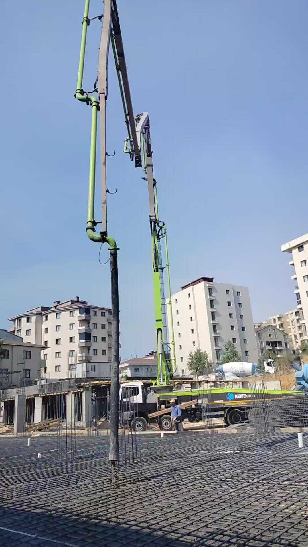 A concrete pump truck pours concrete onto rebar at a building construction site under a clear sky.