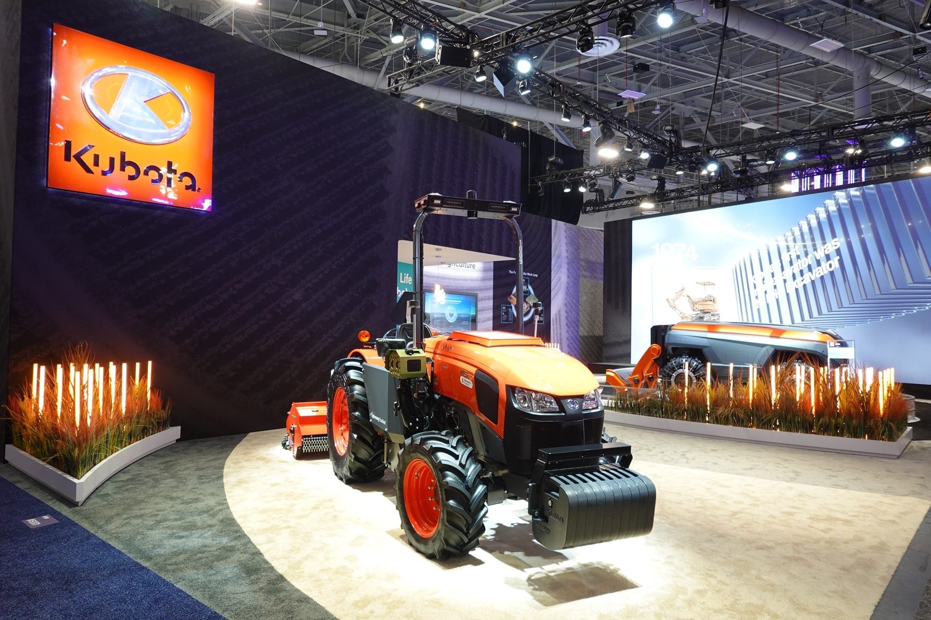 Kubota exhibition booth featuring an orange tractor, other farming equipment, and a large illuminated logo.