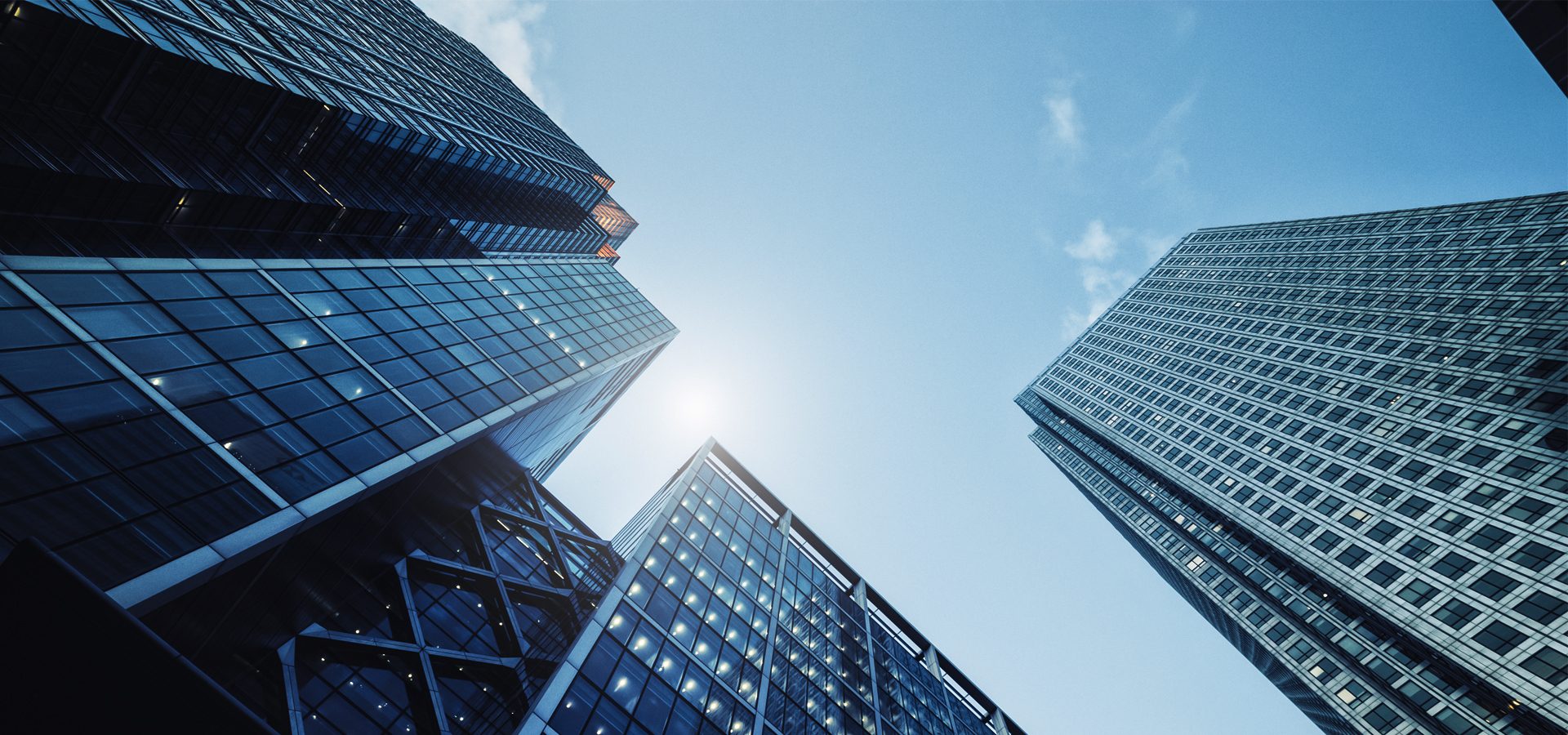 Low-angle view of modern glass skyscrapers under a bright blue sky with sunlight.