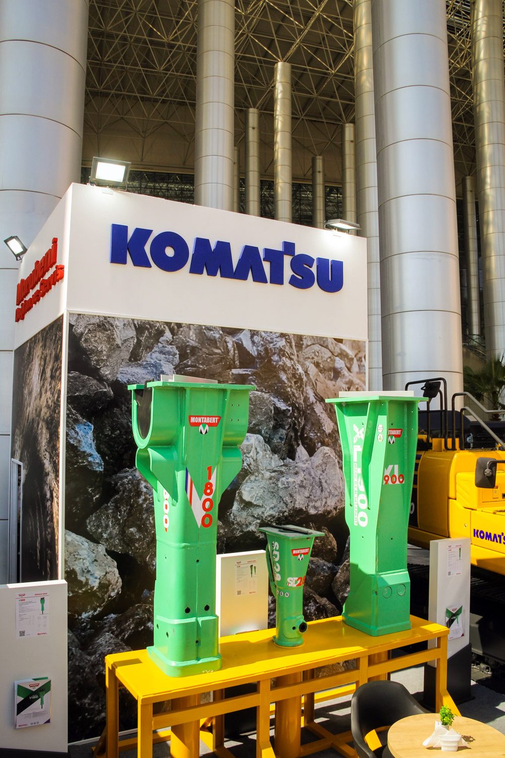 Komatsu exhibition booth with green Montabert hydraulic breakers on a yellow display table.