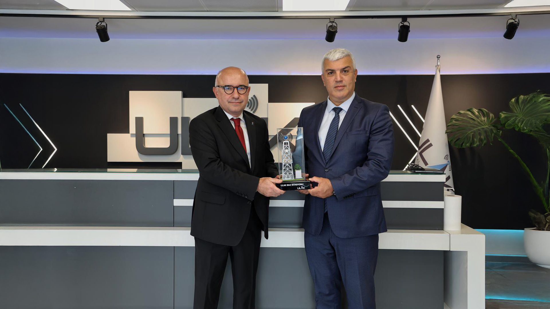 Two men holding a base station trophy with ULAK logo in background.