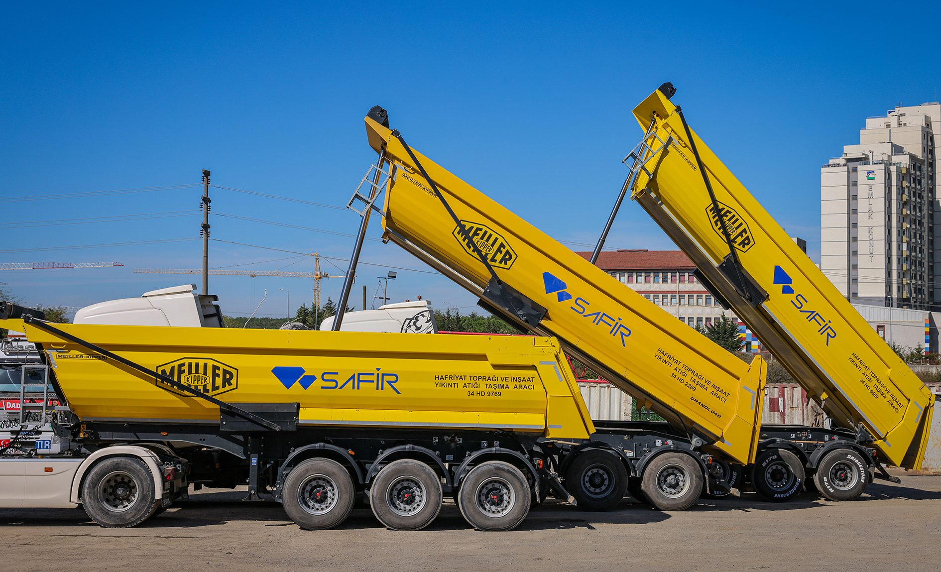 Three yellow dump trucks, two with raised beds, under a clear blue sky.