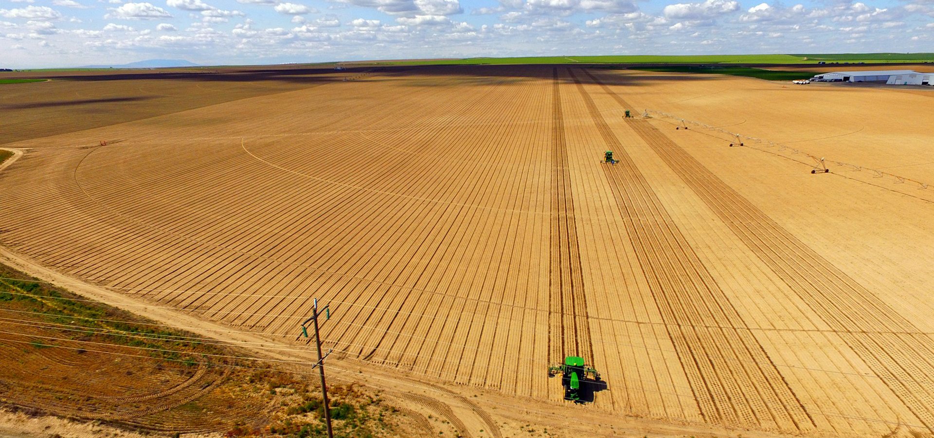 Farm field with tractors planting rows and an irrigation system.