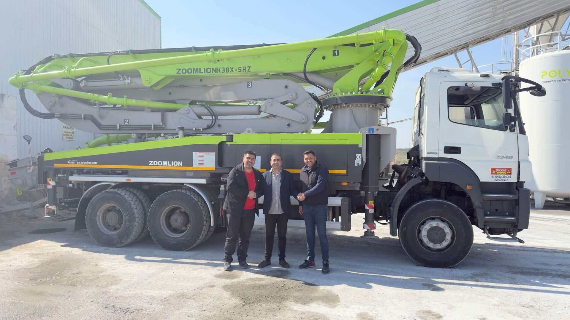 Three men shake hands in front of a new green and black Zoomlion concrete pump truck, marking a business agreement.