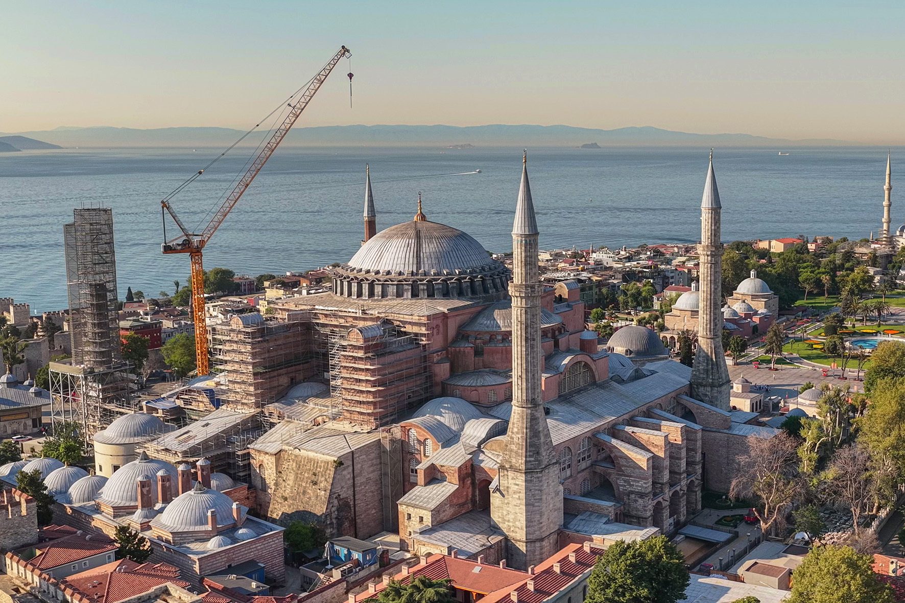 Hagia Sophia, with scaffolding and a crane, overlooks the sea and distant land under a clear sky.