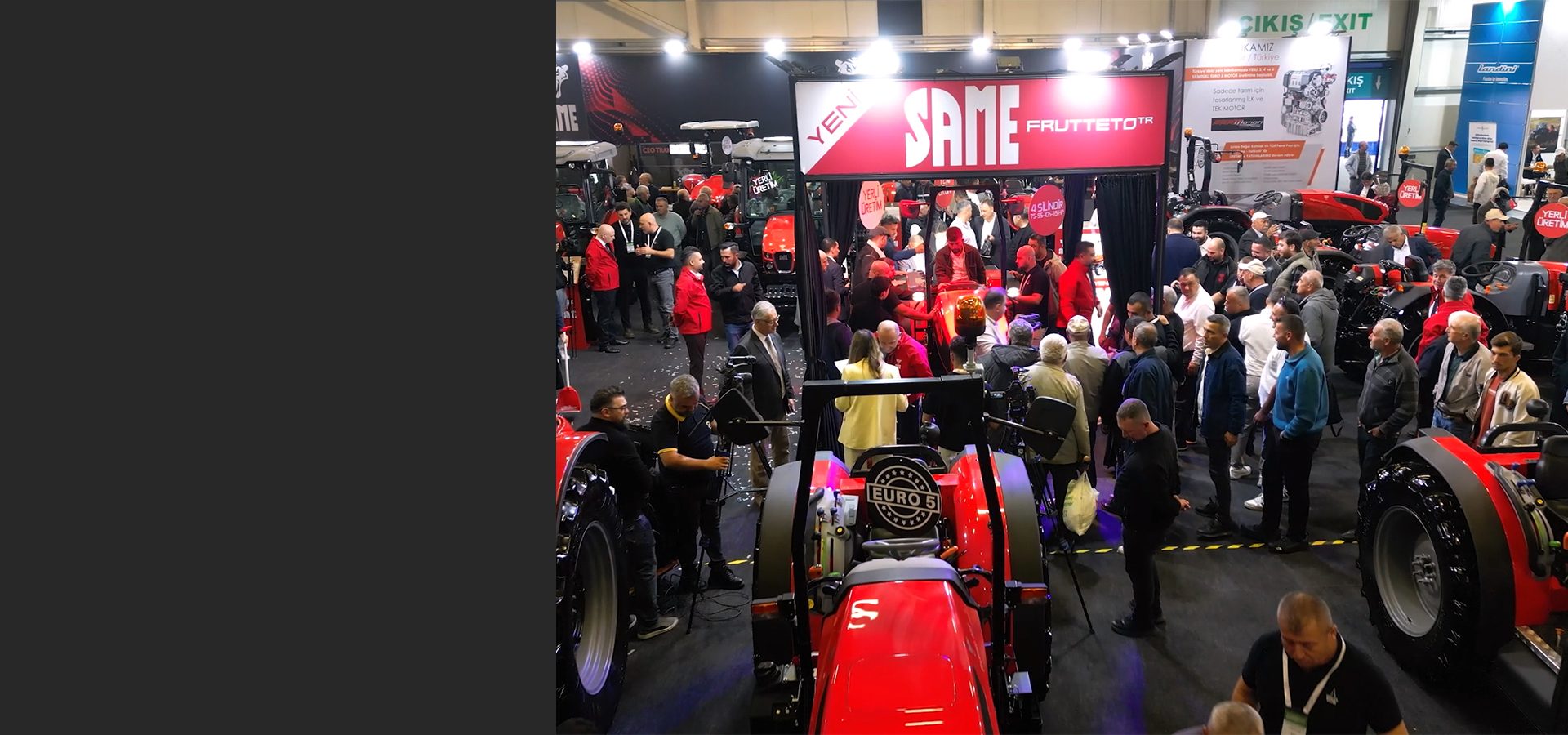 Indoor trade show featuring red SAME FRUTTETO TR tractors and many attendees.