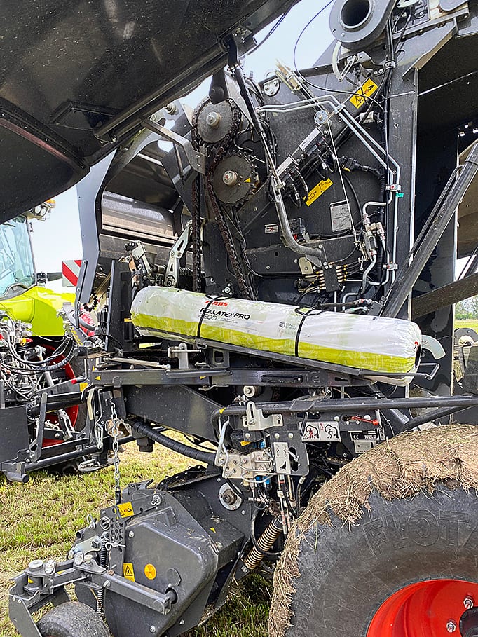 A baler's internal mechanics with chains, gears, hydraulics, and a Follatex Pro film roll.