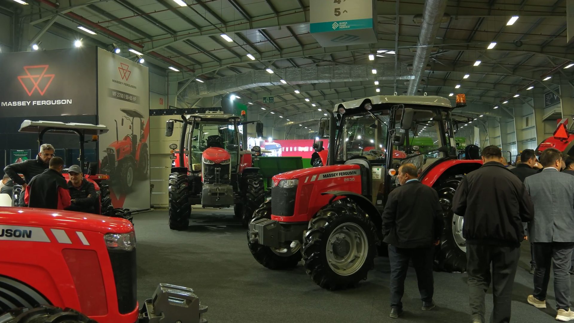Indoor exhibition of red Massey Ferguson tractors with visitors.