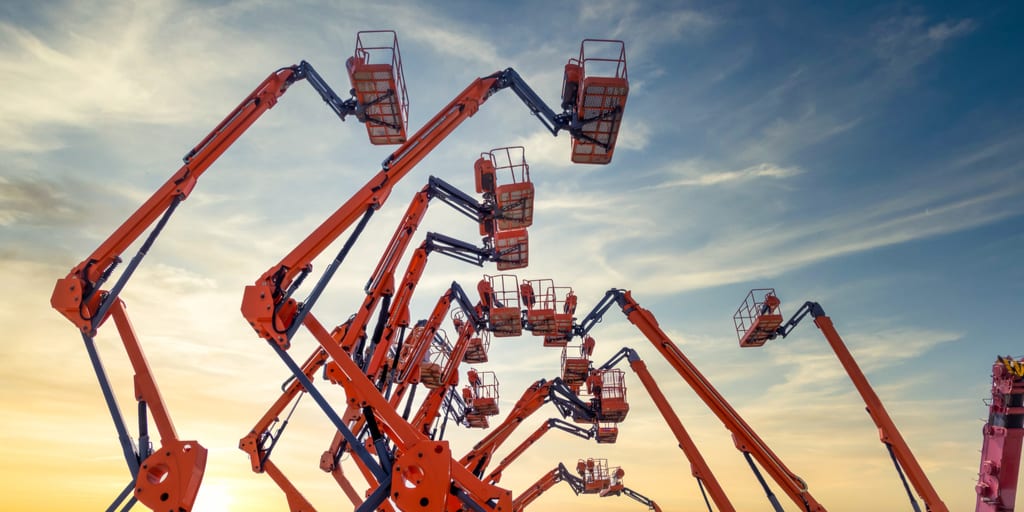 Orange boom lifts and baskets against a cloudy sky.