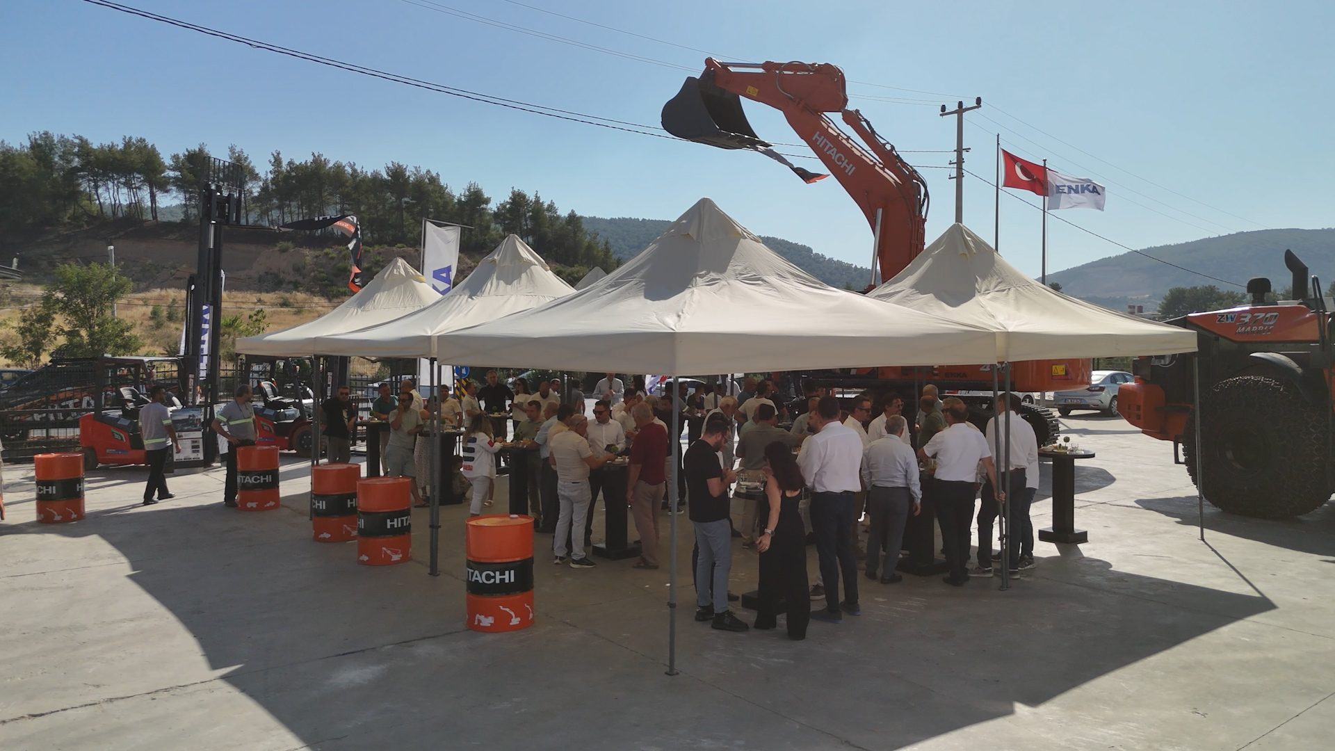 Hitachi machinery exhibition with people under tents and a Turkish flag.
