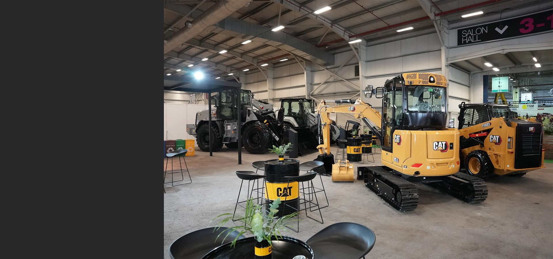 CAT construction vehicles: excavators, loaders, and a skid steer, displayed in an exhibition hall.