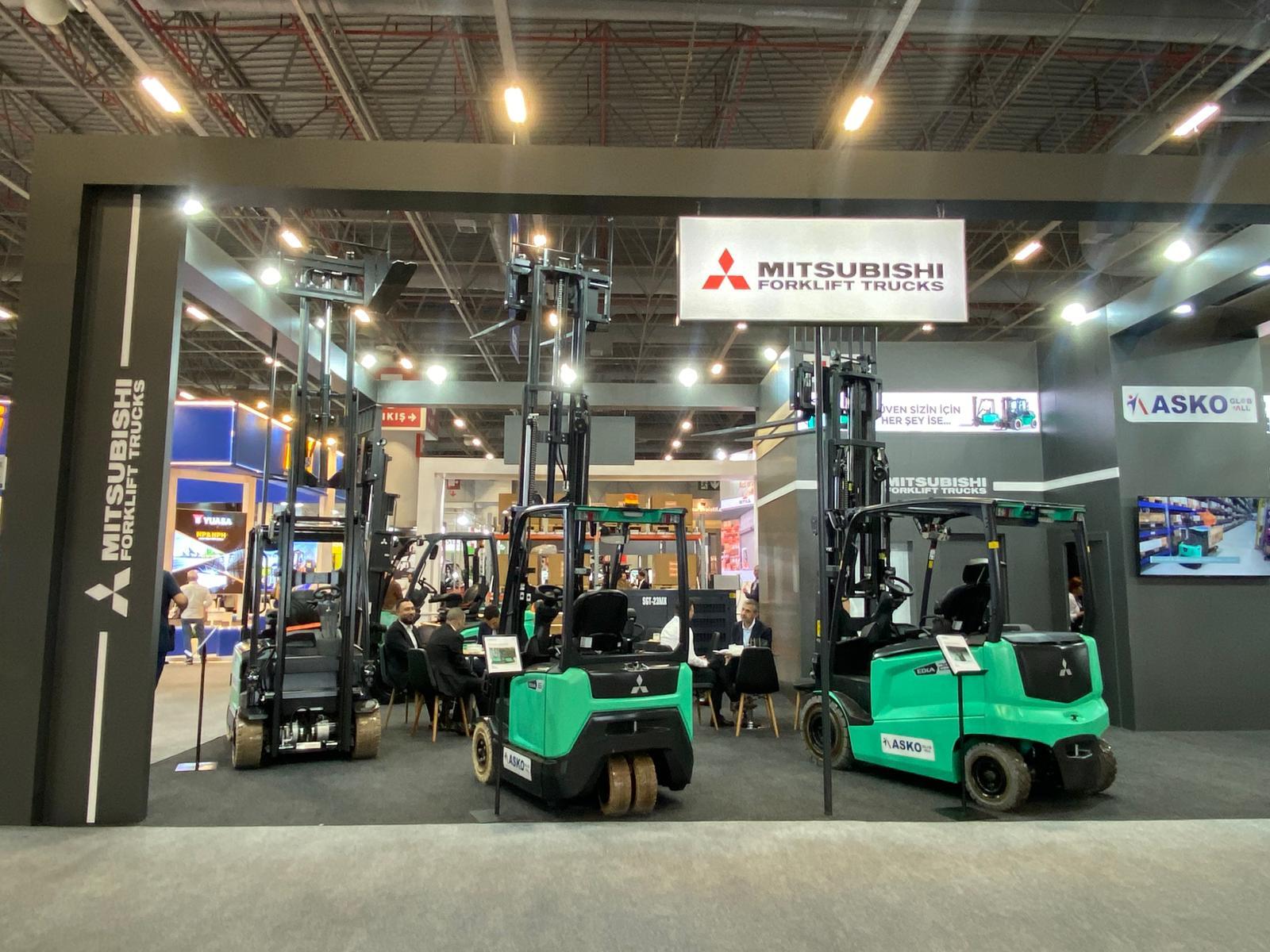 Mitsubishi Forklift Trucks booth with green forklifts and visitors at an exhibition.